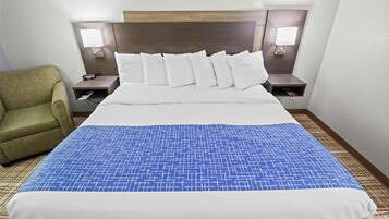A hotel room with a large bed, a green armchair, two bedside tables with lamps, and a patterned bedspread.
