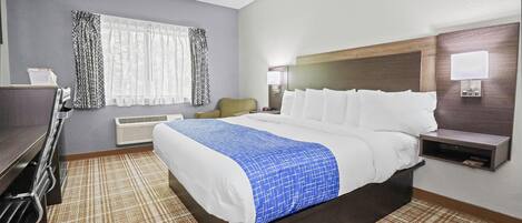 Une chambre d’hôtel avec un grand lit, un bureau, une chaise, une fenêtre avec des rideaux, une table de chevet et une lampe.