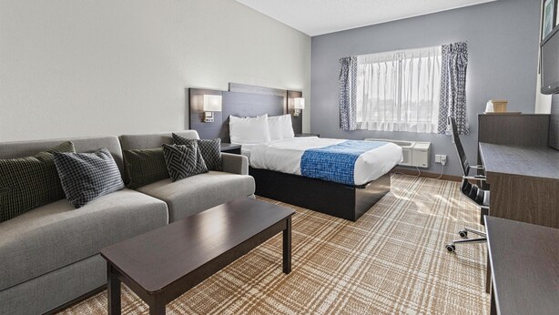 A modern hotel room with a bed, sofa, desk, and a large window with curtains. - GrandStay Hotel & Suites  (Minocqua)
