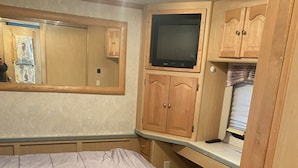 Een slaapkamer met een bed, houten kasten, een televisie en een spiegel.