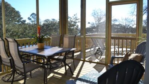 A covered outdoor area with a table and chairs, a potted plant, and a view of trees and a building in the background.