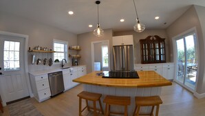 A modern kitchen with white cabinetry, a stainless steel refrigerator, wooden stools, and pendant lighting.