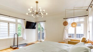 Un dormitorio con una cama grande, un calefactor portátil, un televisor montado en la pared y un balcón con vistas.