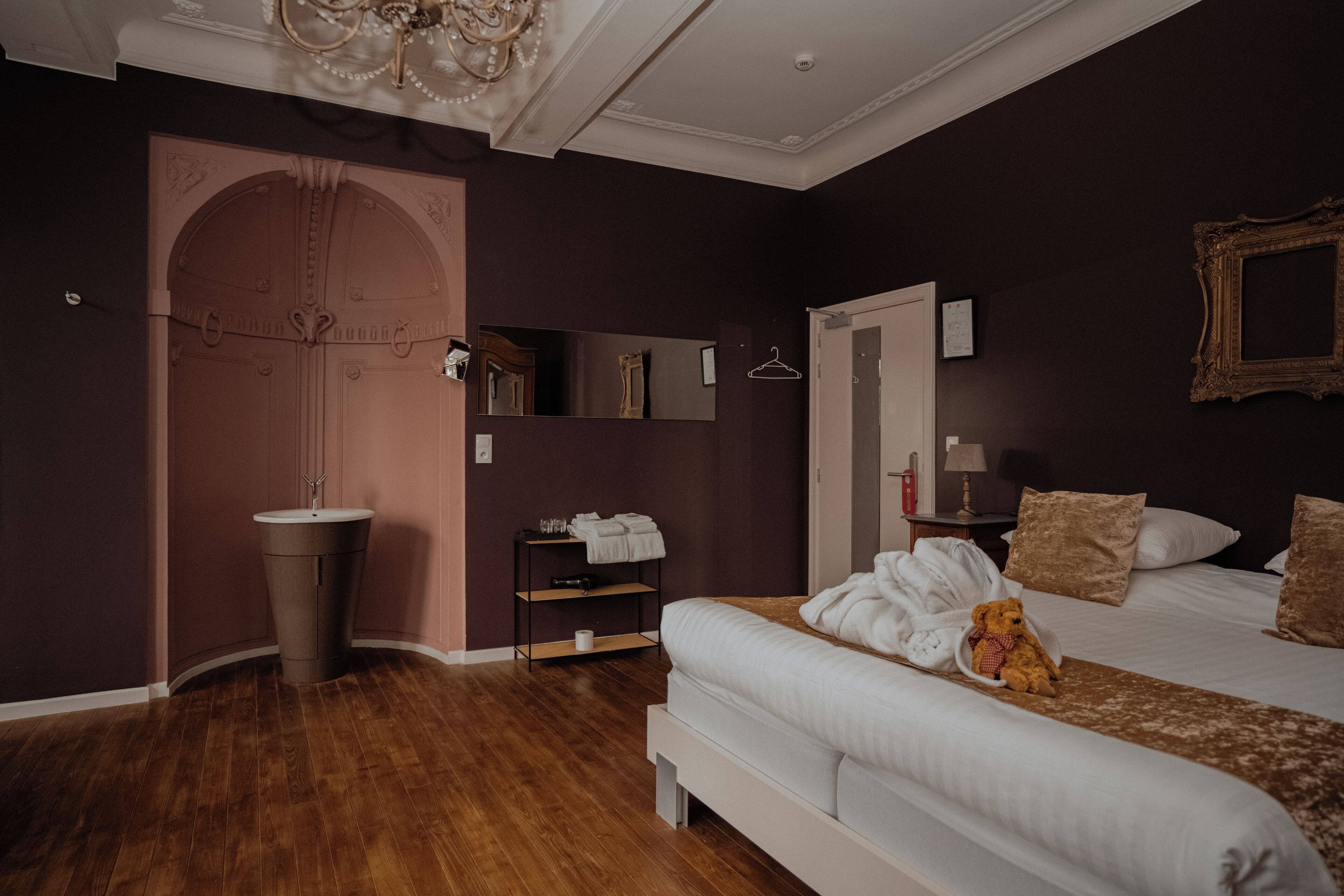 A bedroom with a large bed, a bedside table, a mirror, a wardrobe, and a chandelier.