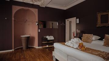A bedroom with a large bed, a bedside table, a mirror, a wardrobe, and a chandelier.