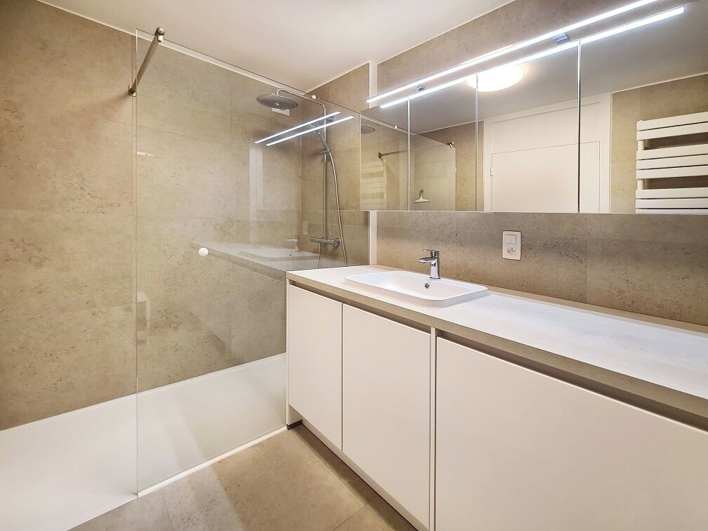Een moderne badkamer met een douchecabine van glas, een witte wastafel en een grote spiegel.