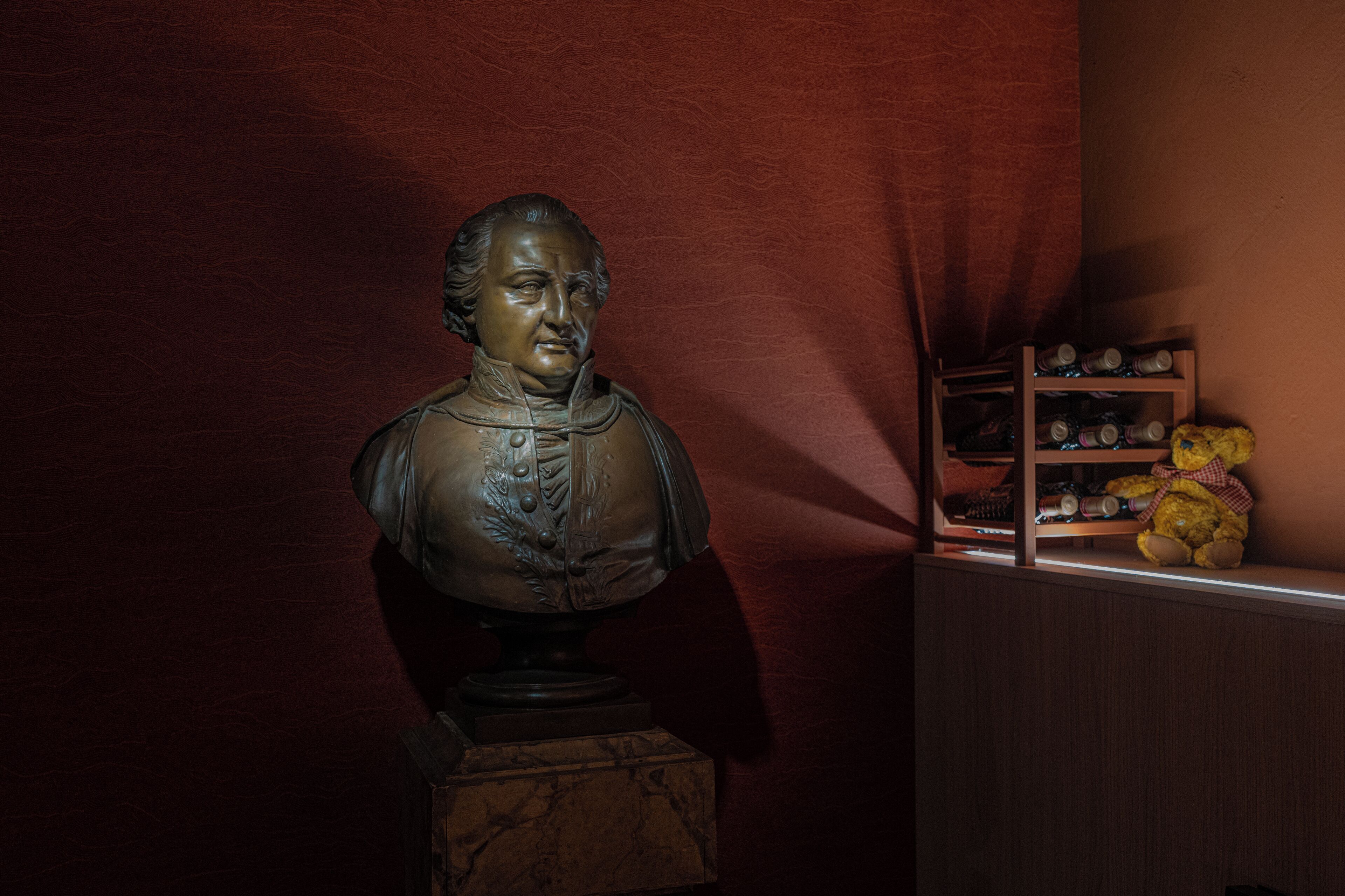 Un busto sobre un pedestal frente a un fondo rojo.