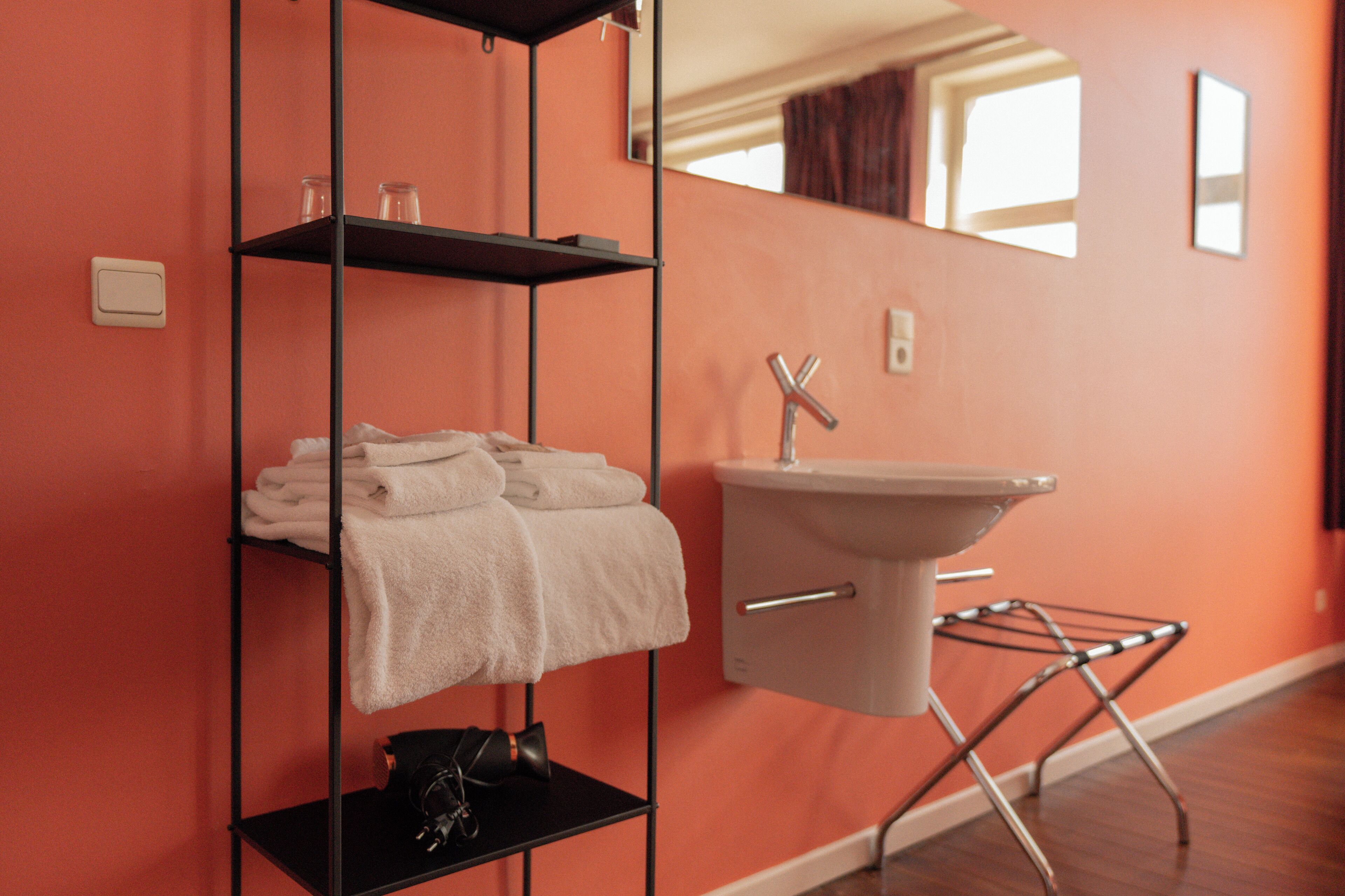 Een badkamer met een zwarte metalen plank met handdoeken, een witte wastafel met een chroomkraan en een spiegel aan de muur.