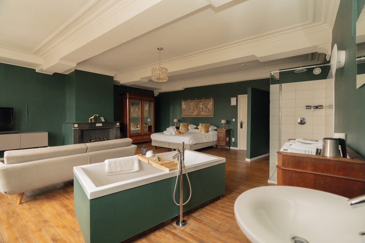 Une chambre d’hôtel moderne équipée d’un canapé, d’un petit coin cuisine avec un évier, d’un lit, d’une salle de bain avec douche et d’une télévision.
