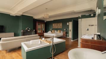 A modern hotel room with a sofa, a small island with a sink, a bed, a bathroom with a shower, and a TV.