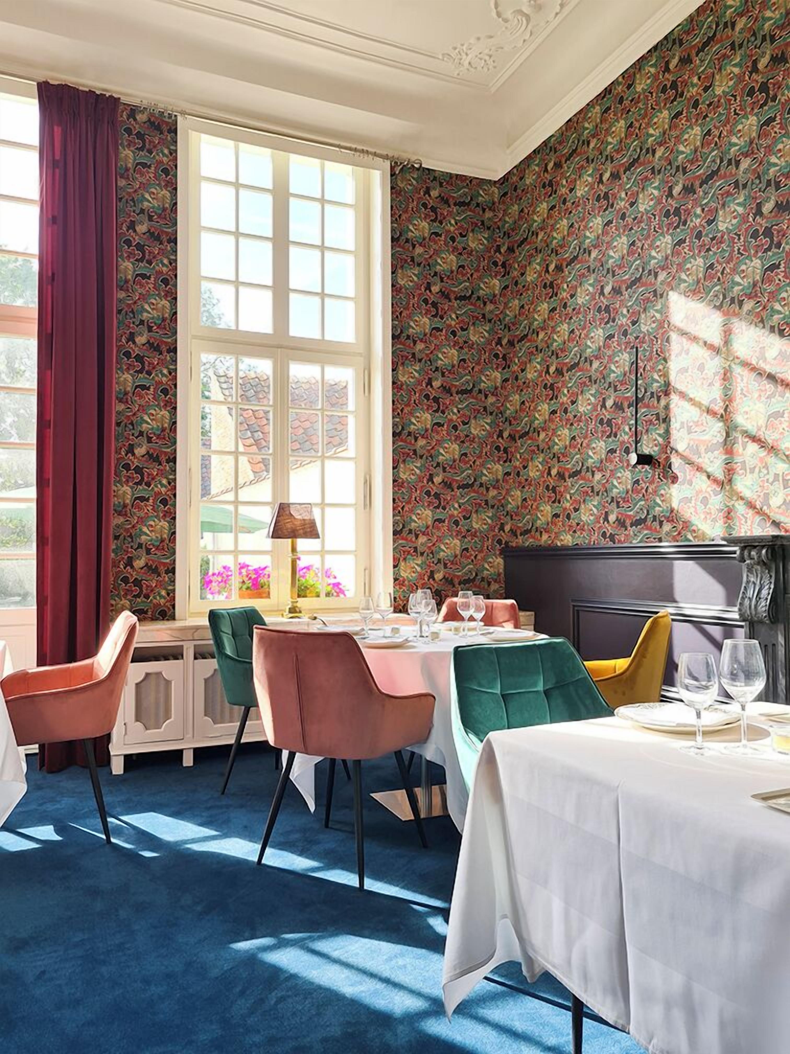 Een eetgedeelte met een groot raam, behang met een patroon en moderne stoelen.