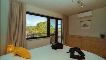 A hotel room with a large window, a bed, a bedside lamp, and a wooden dresser.