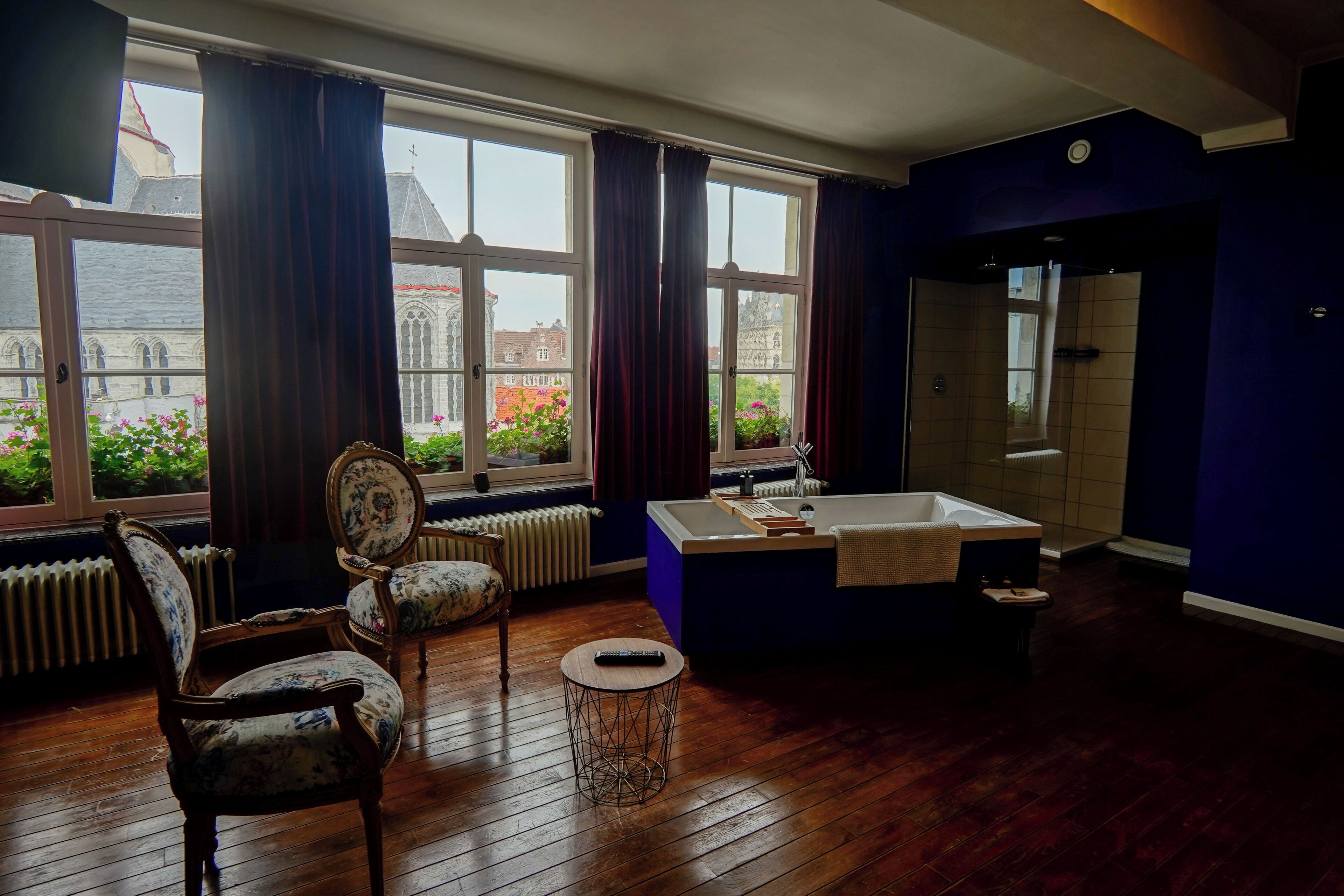 A room with a large window, a bathtub, and two chairs.