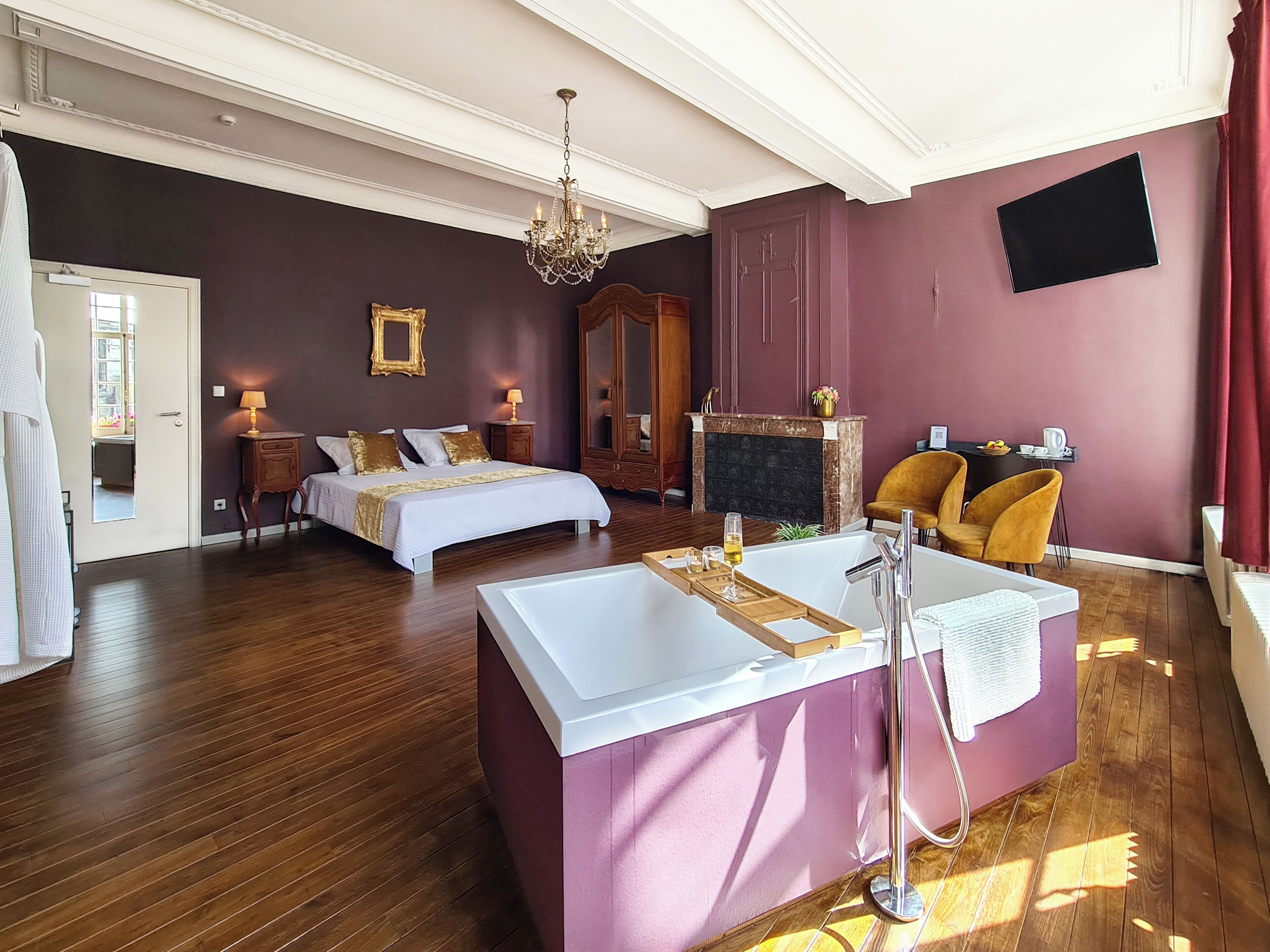 A hotel room with a large bed, a separate bathroom with a bathtub, a fireplace, and a dining area with chairs.