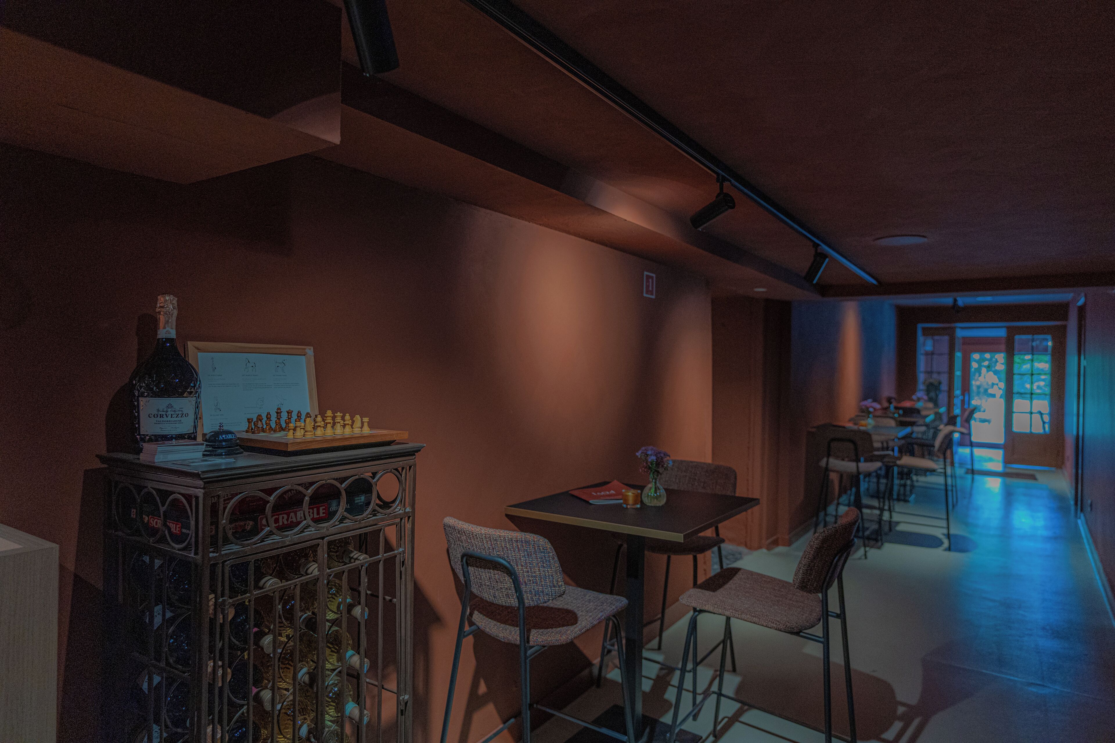 A dimly lit room with a chessboard, a bottle, and a menu on a table. There are chairs and a bar area in the background.