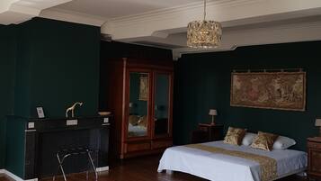 A spacious bedroom with a large bed, a sitting area with a desk, a wardrobe, and a large bathtub.