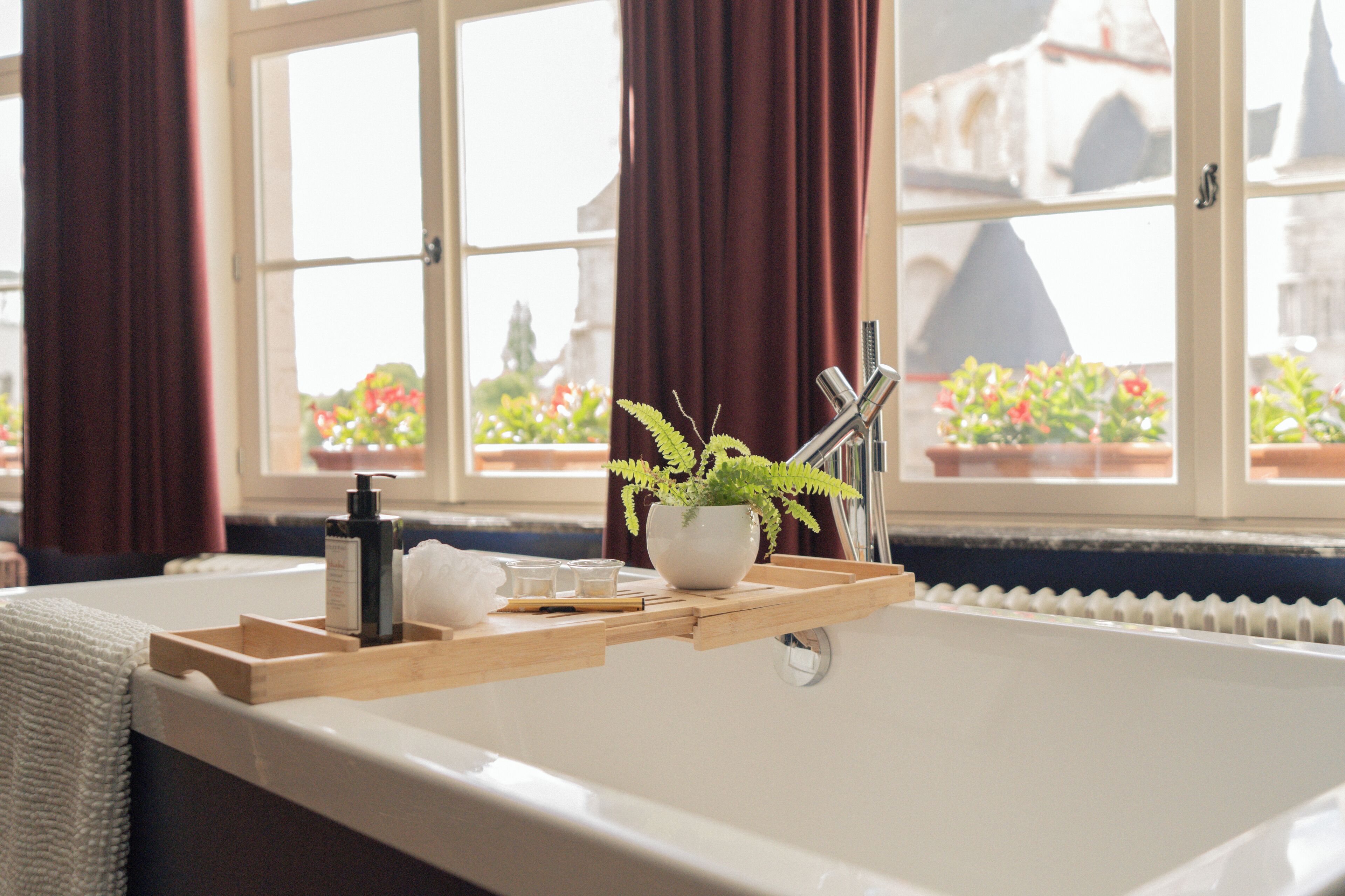 Une salle de bain avec une baignoire, une fenêtre avec des rideaux, une plante et des articles de toilette.