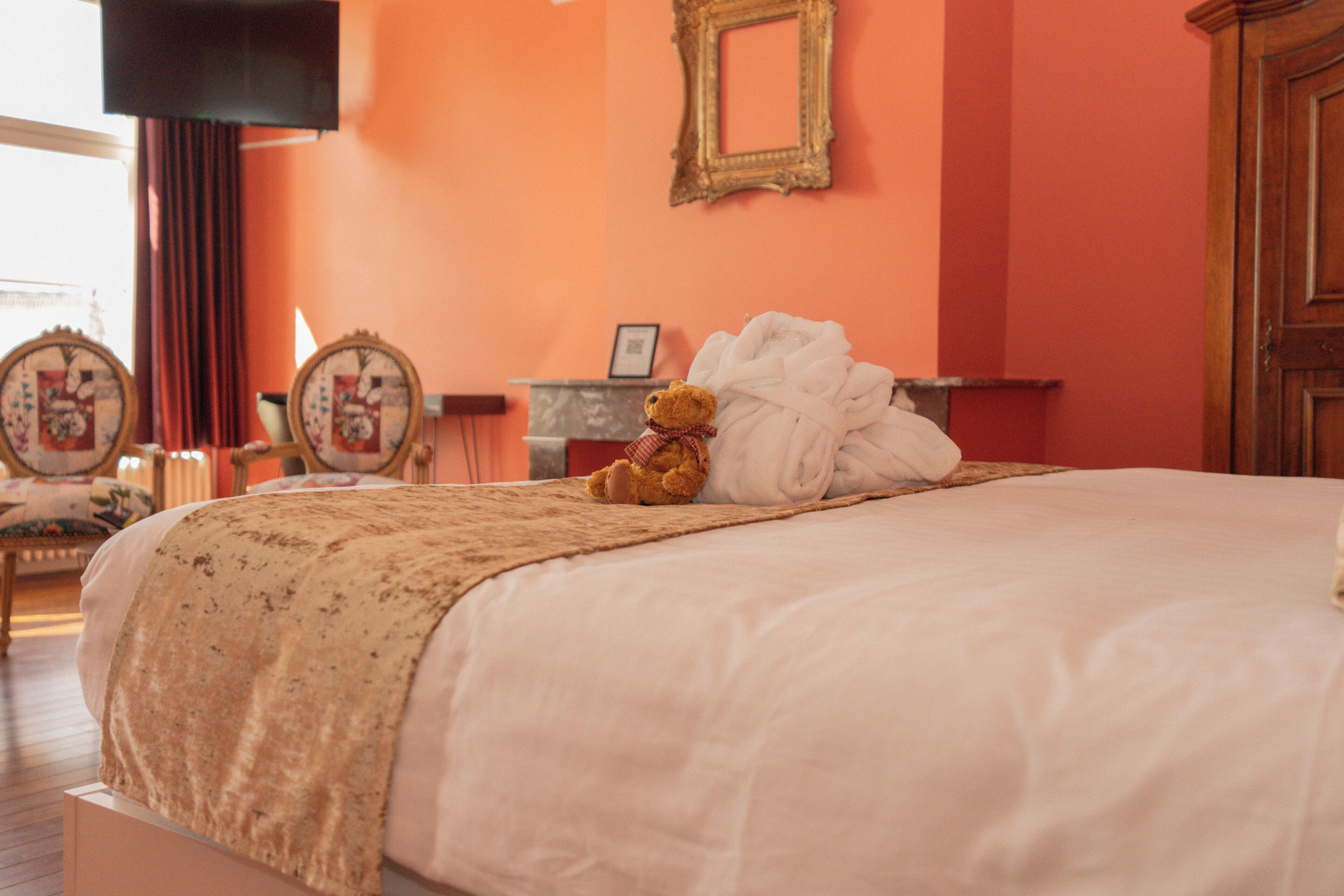 A neatly made bed with a teddy bear and a folded towel on it, a wooden cabinet, and a framed picture on the wall.