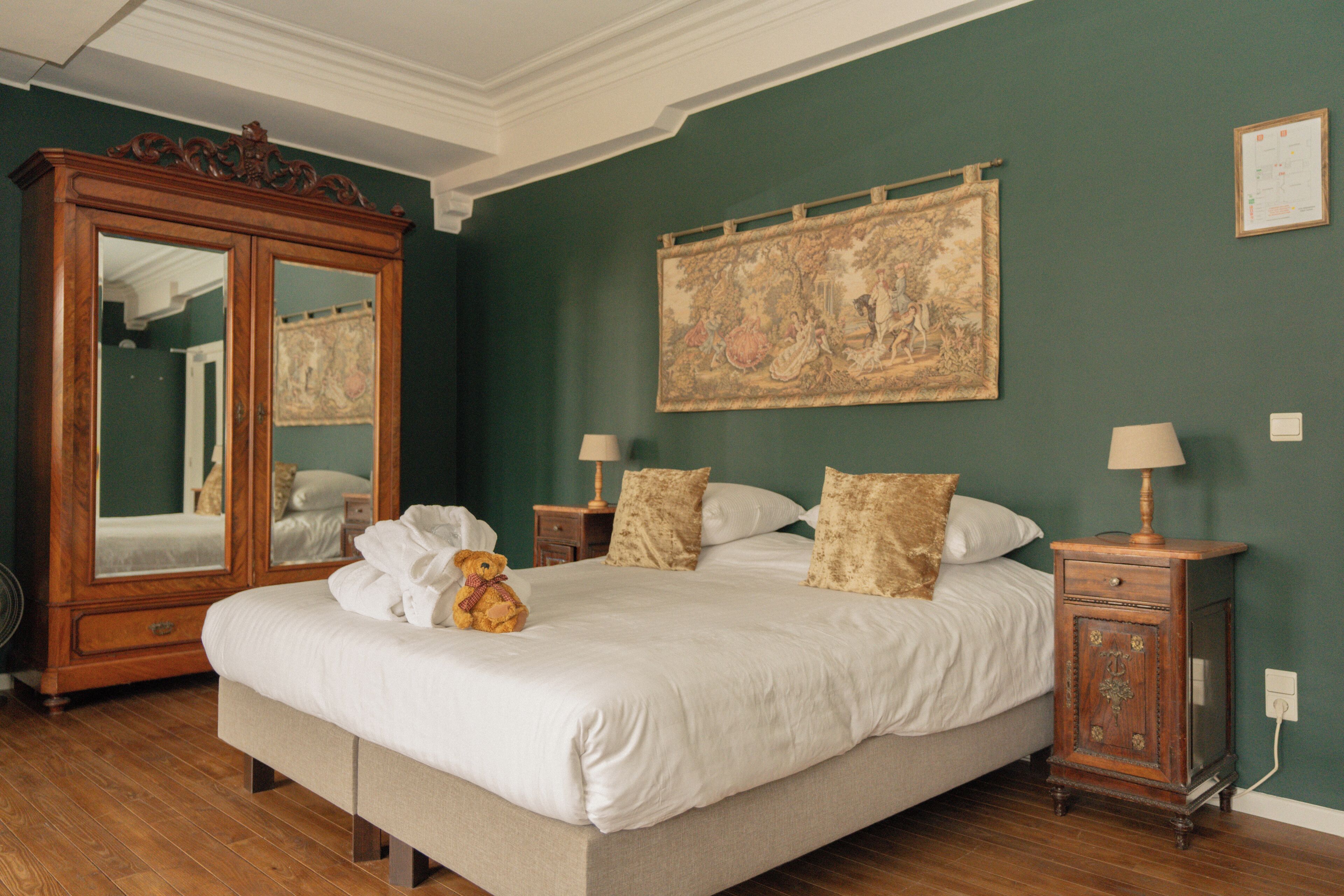 Una camera da letto con un letto grande, un armadio in legno, uno specchio, un comodino e un arazzo appeso al muro.