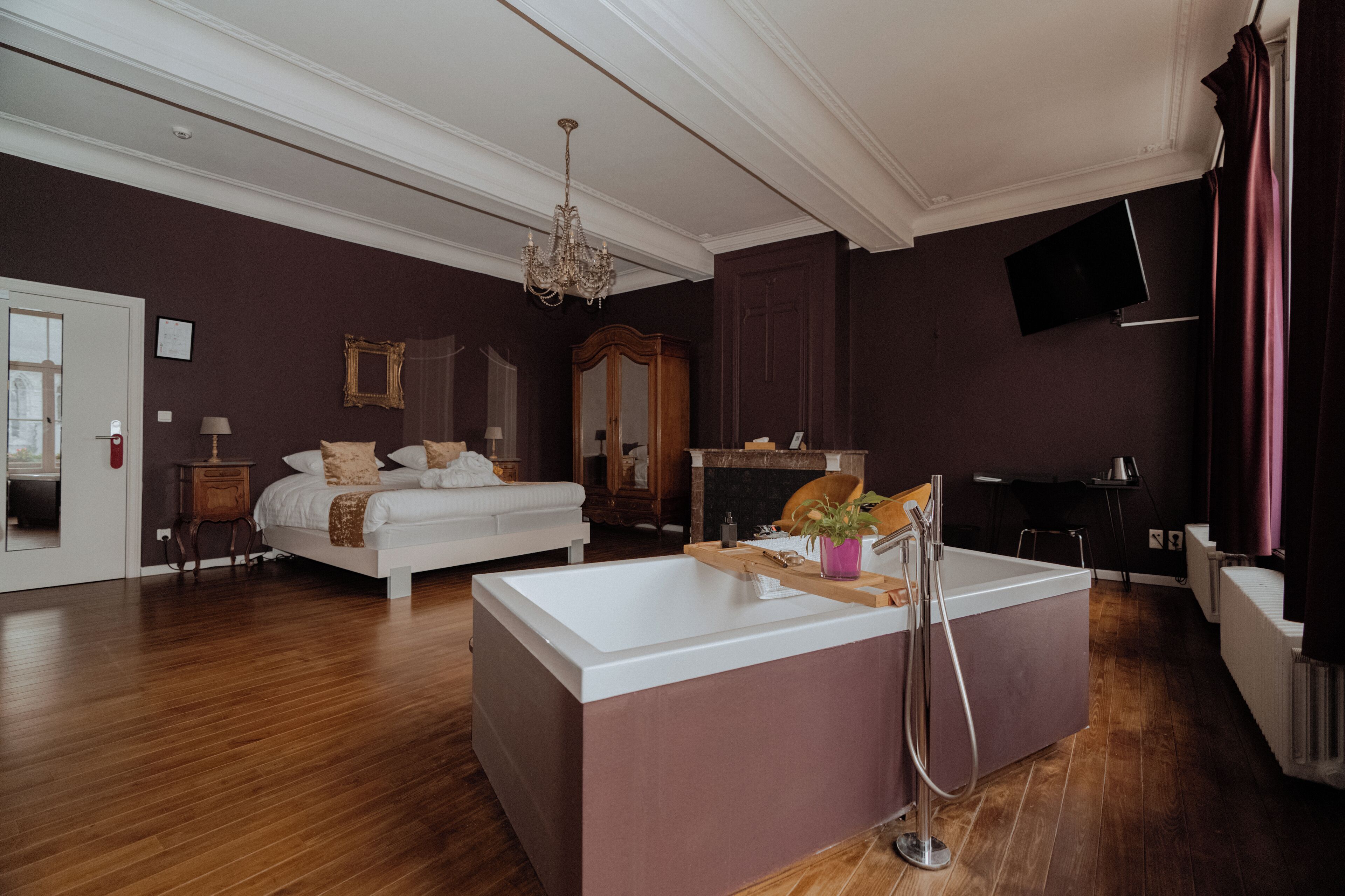A modern bedroom with a large bed, a bathtub, and a chandelier.