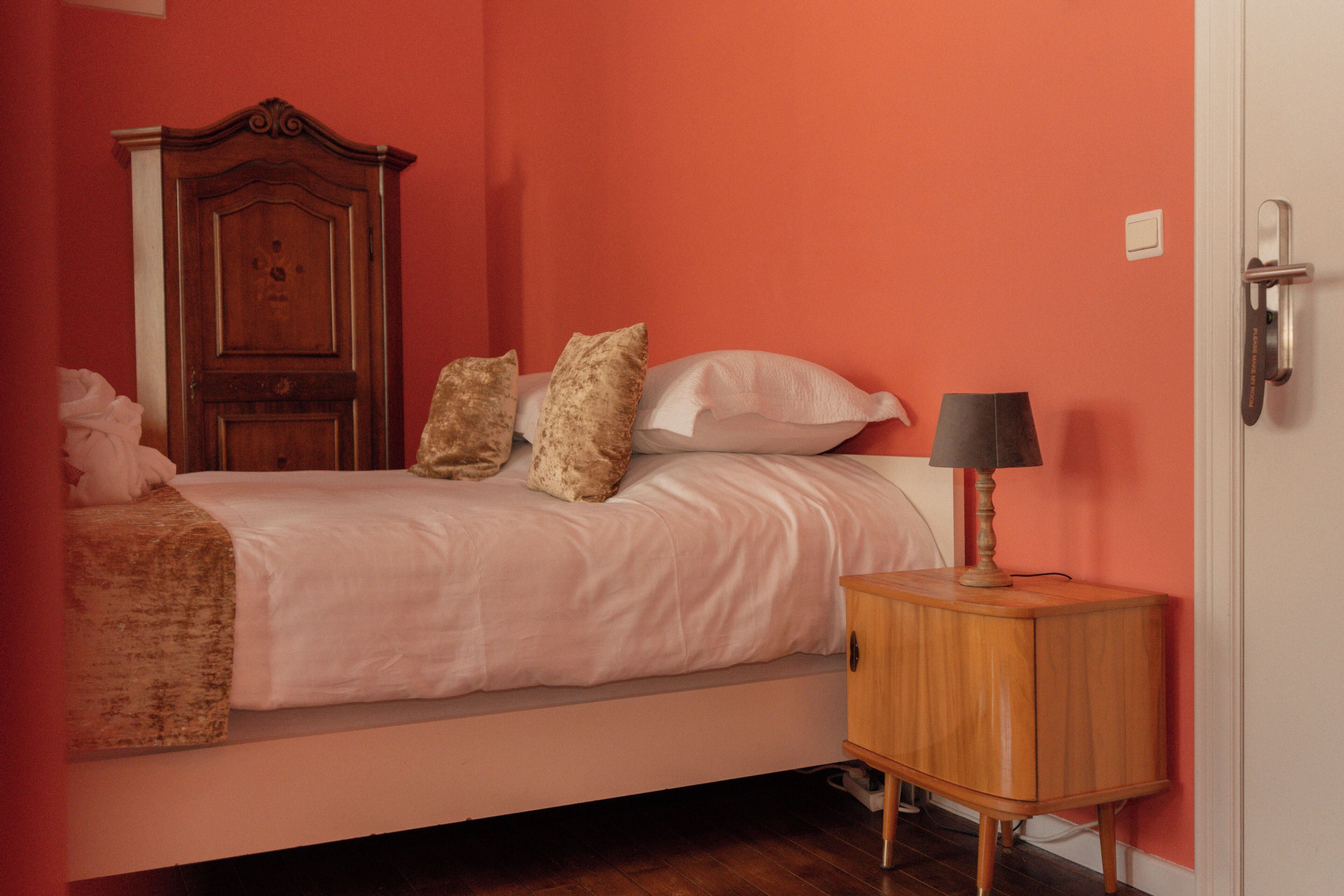 Un dormitorio con cama, almohadas, una mesita de noche de madera y una puerta.