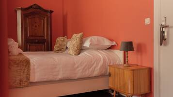 Un dormitorio con cama, almohadas, una mesita de noche de madera y una puerta.