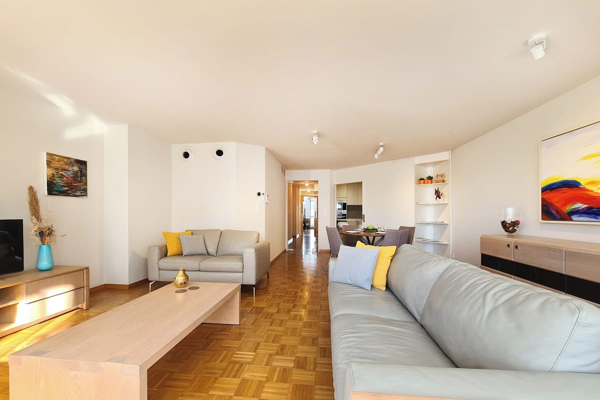 Un salon moderne avec un canapé, une table basse et un meuble pour la télévision. On aperçoit un coin repas à l’arrière-plan.