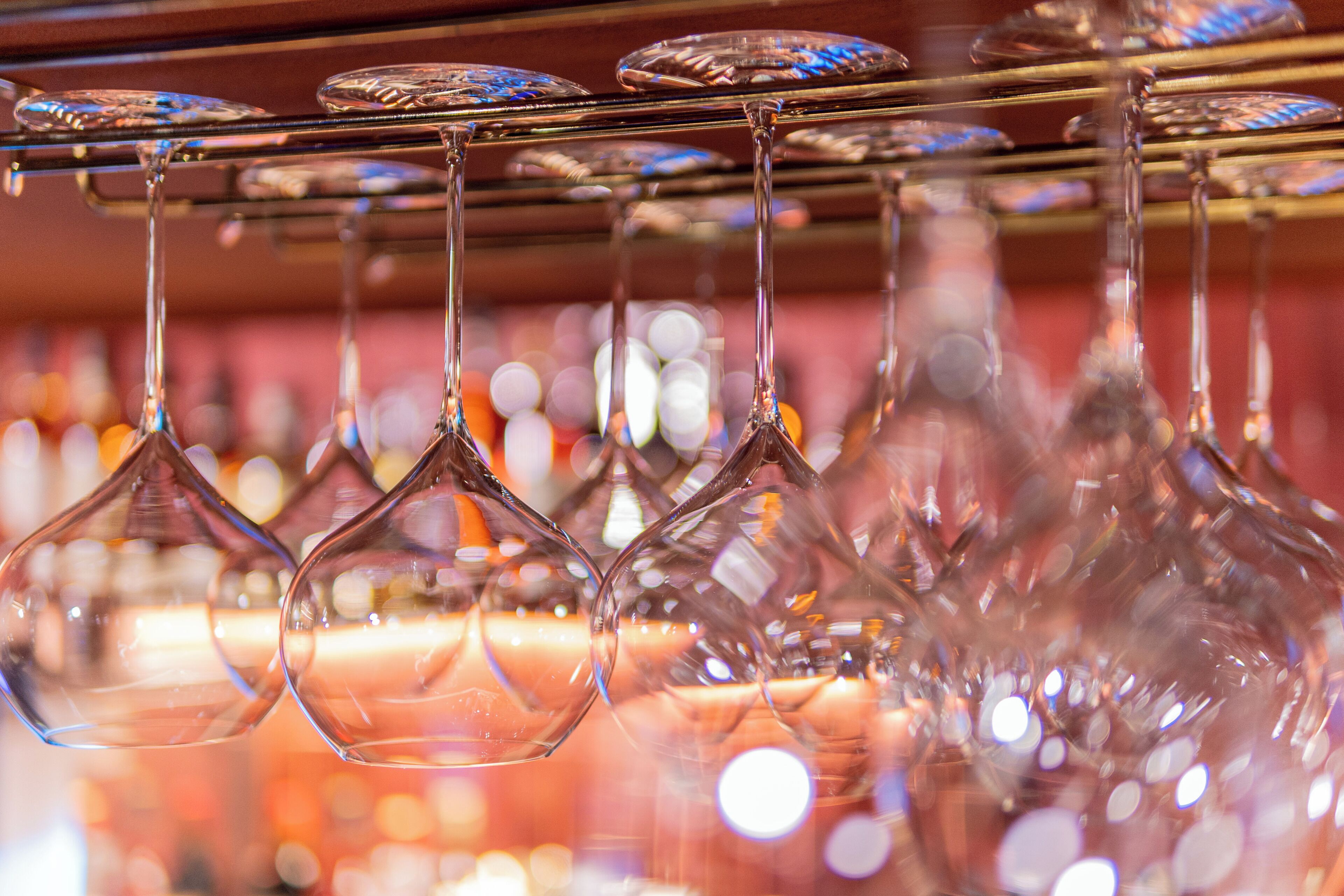 A row of hanging wine glasses with a blurred background of lights.