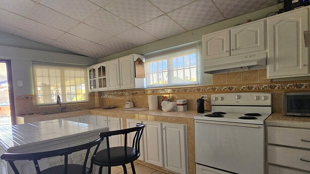 Una cocina con gabinetes blancos, una estufa y un comedor con dos taburetes.