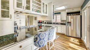 A modern kitchen with white cabinetry, a stainless steel refrigerator, and a bar area with patterned chairs. - Lakefront Hot Springs Village Home w/ Private Dock (Hot Springs)