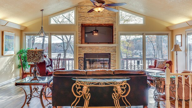 A spacious living room with a fireplace, large windows, and a ceiling fan. - Lakefront Hot Springs Village Home w/ Private Dock (Hot Springs)