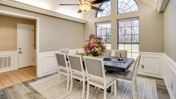 A dining room with a high ceiling fan, a dining table with chairs, a vase of flowers, and large windows. - Large Yard, Fire Pit & Games: Grandview Haven! (Grandview)