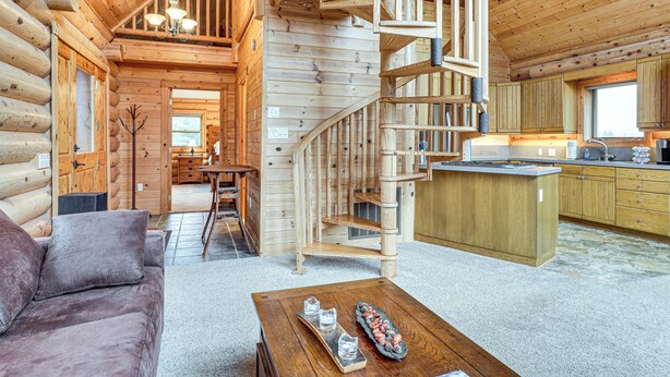A log cabin interior with a wooden staircase, a dining area, and a kitchen.