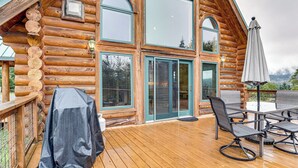 A wooden log cabin with a deck, outdoor seating, and a covered grill area.