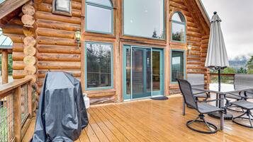 Une cabane en bois avec une terrasse, un espace salon extérieur et un coin barbecue couvert.
