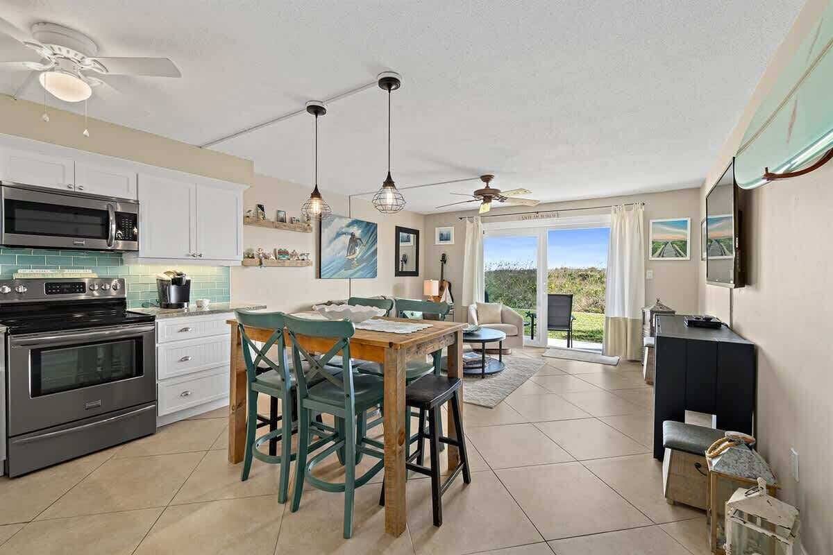 A modern kitchen with stainless steel appliances, a dining area with wooden chairs, and a large sliding glass door leading to a patio.