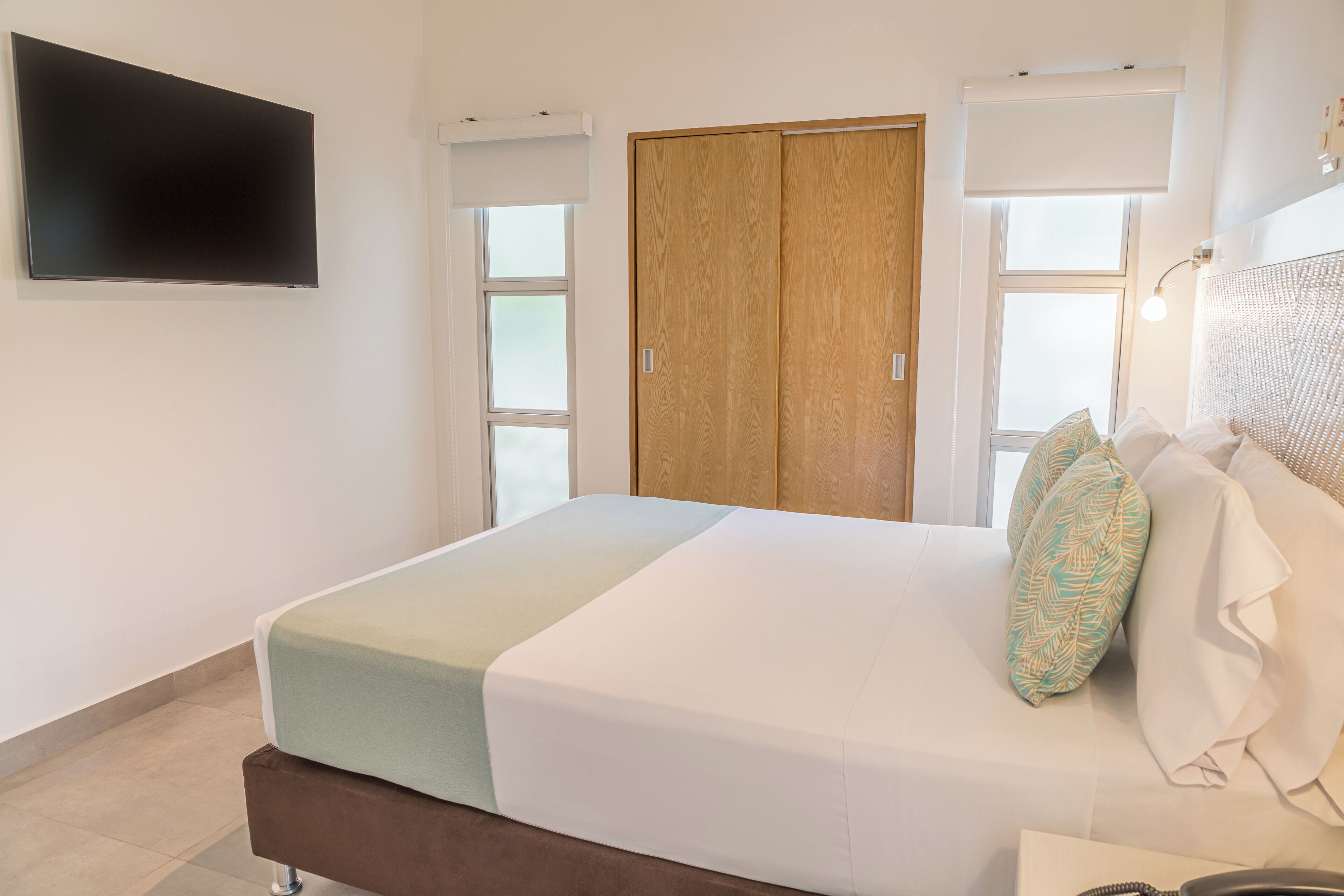 Un dormitorio con cama, televisor montado en la pared y armario de madera.
