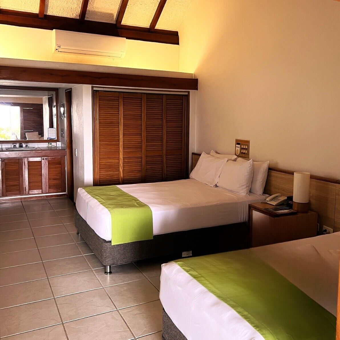 Habitación de hotel con cama, mesita de noche y baño con lavamanos y espejo.