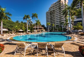 Una piscina con sillas de descanso y palmeras, rodeada por un edificio alto.