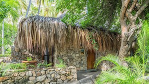 A rustic stone building with a thatched roof, a wooden door, and a stone wall with a small garden area.