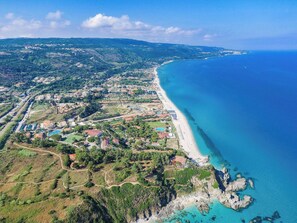 An aerial view of a coastal town with a long beach, residential areas, and a mix of natural and developed landscapes.