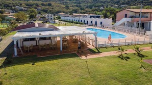 A pool area with a covered seating area, surrounded by buildings and a hilly landscape. - Appartamenti Standard (Zambrone)