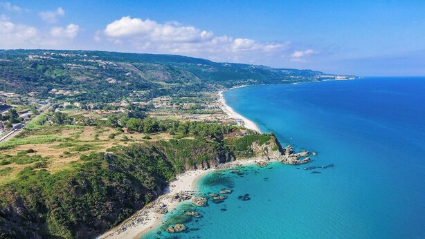 An aerial view of a coastal area with a beach, rocky outcrops, and a densely vegetated hillside. - Appartamenti Standard (Zambrone)