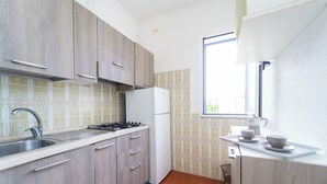 A kitchen with wooden cabinets, a white refrigerator, a sink, and a window providing natural light. - Appartamenti Standard (Zambrone)
