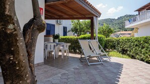 A covered patio with a table and chairs, a lounge chair, and a view of a hillside. - Appartamenti Standard (Zambrone)