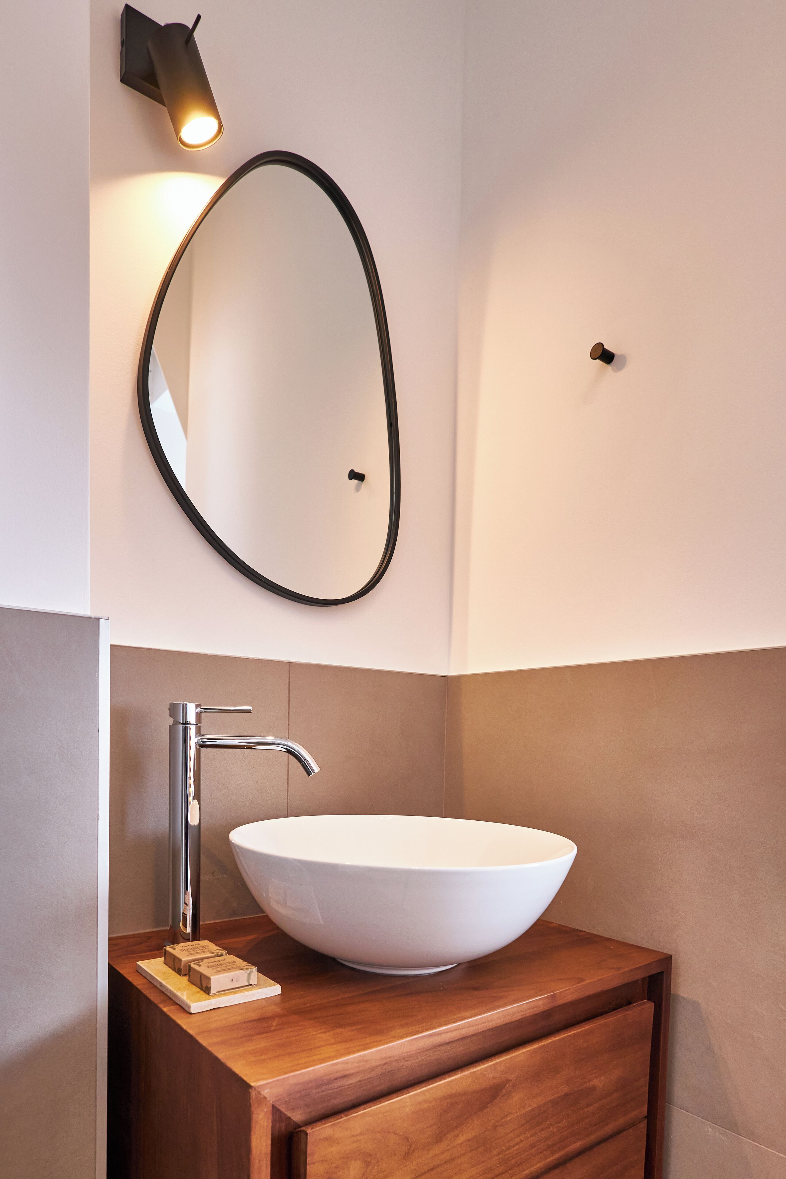 A modern bathroom with a large oval mirror, a white vessel sink, and a wooden vanity.