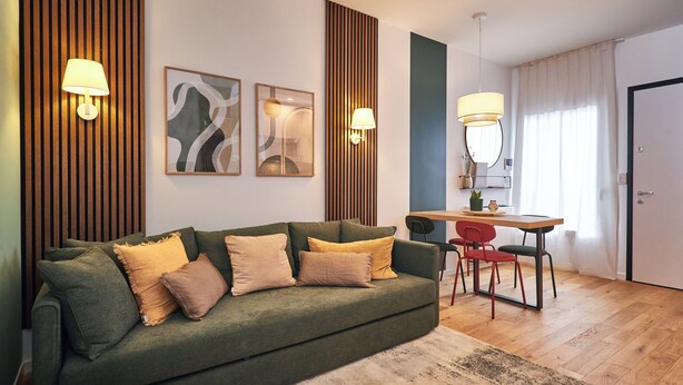 A modern living room with a green sofa, two wall-mounted lamps, abstract art, a wooden accent wall, and a dining area with a table and chairs. - Orti29 Luxury Stay. A cozy home within walking distance of the center of Bologna (Bologna)