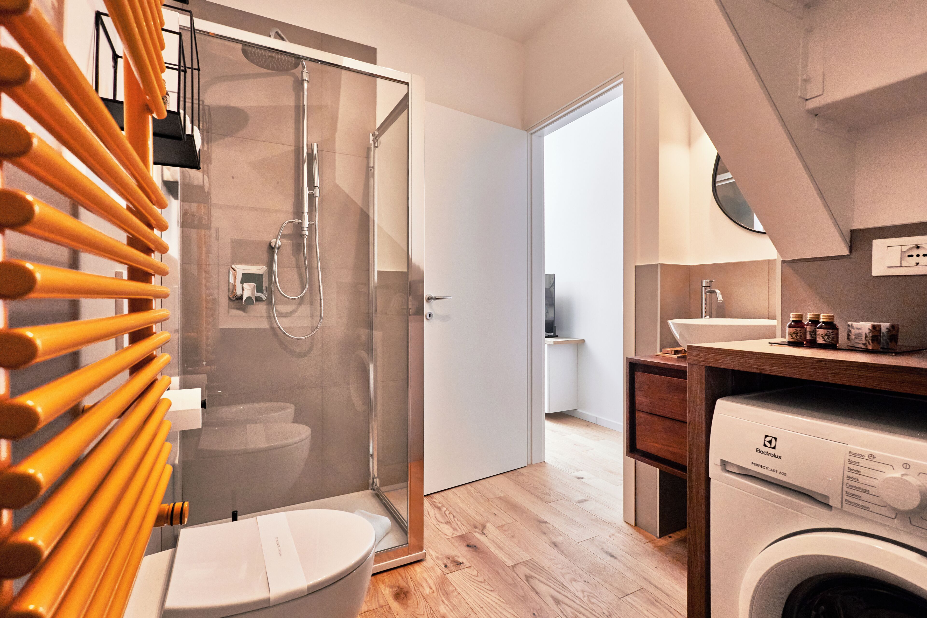 A modern bathroom with a glass shower enclosure, a toilet, and a washing machine.