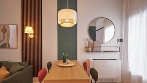A modern living room with a wooden dining table, colorful chairs, a green sofa, a wall-mounted mirror, and a hanging pendant light. - Orti29 Luxury Stay. A cozy home within walking distance of the center of Bologna (Bologna)