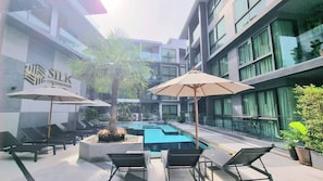 A modern building with a swimming pool, lounge chairs, and umbrellas. - B307 - 1 Bedroom Condo Pool View Near Ao Nang Beach (Krabi)